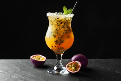 Photo of Tasty passion fruit drink with mint in glass and fresh fruits on dark gray textured table against black background