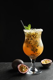 Photo of Tasty passion fruit drink with mint in glass and fresh fruits on dark gray textured table against black background