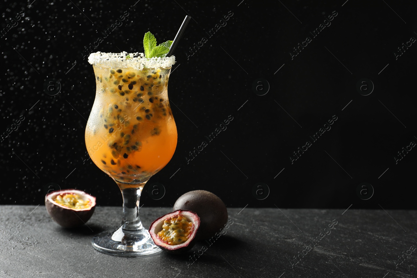 Photo of Tasty passion fruit drink with mint in glass and fresh fruits on dark gray textured table against black background. Space for text