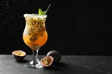 Photo of Tasty passion fruit drink with mint in glass and fresh fruits on dark gray textured table against black background. Space for text