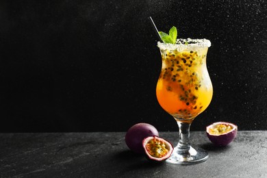Photo of Tasty passion fruit drink with mint in glass and fresh fruits on dark gray textured table against black background. Space for text
