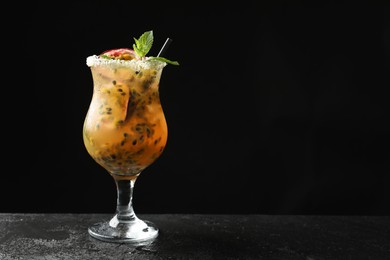 Photo of Tasty passion fruit drink with mint in glass on dark gray textured table against black background. Space for text