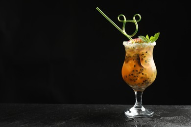 Photo of Tasty passion fruit drink with mint in glass on dark gray textured table against black background. Space for text