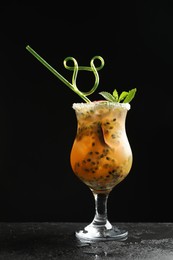 Photo of Tasty passion fruit drink with mint in glass on dark gray textured table against black background