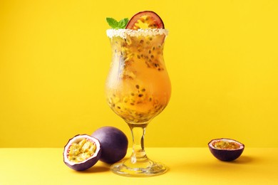 Photo of Tasty passion fruit drink with mint in glass and fresh fruits on yellow background