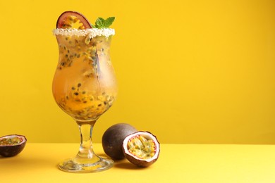 Photo of Tasty passion fruit drink with mint in glass and fresh fruits on yellow background. Space for text