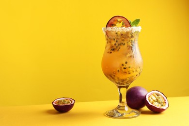 Photo of Tasty passion fruit drink with mint in glass and fresh fruits on yellow background. Space for text