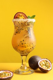 Photo of Tasty passion fruit drink with mint in glass and fresh fruits on yellow background