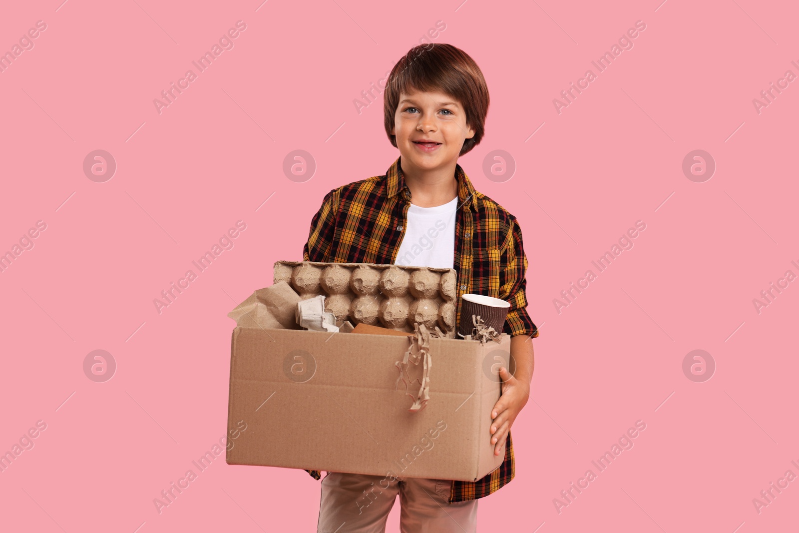 Recycling. Cute little boy with cardboard box full of different waste paper on pink background Photo of Recycling. Cute little boy with cardboard box full of different waste paper on pink background