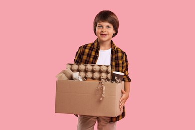 Photo of Recycling. Cute little boy with cardboard box full of different waste paper on pink background