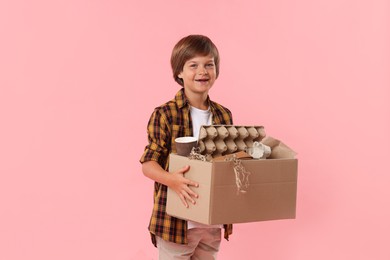 Photo of Recycling. Cute little boy with cardboard box full of different waste paper on pink background