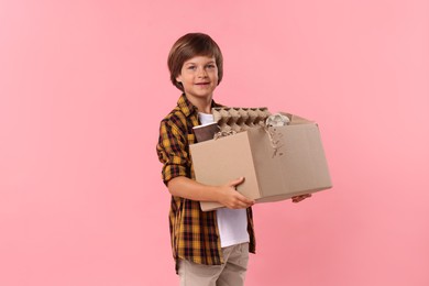 Photo of Recycling. Cute little boy with cardboard box full of different waste paper on pink background
