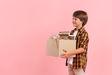 Photo of Recycling. Cute little boy with cardboard box full of different waste paper on pink background, space for text