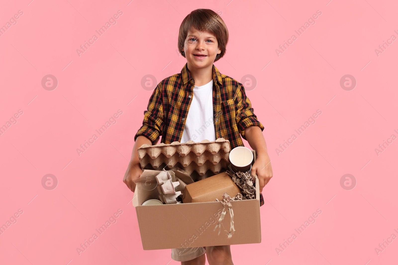 Photo of Recycling. Cute little boy with cardboard box full of different waste paper on pink background