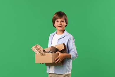Photo of Recycling. Cute little boy with cardboard box full of different waste paper on green background