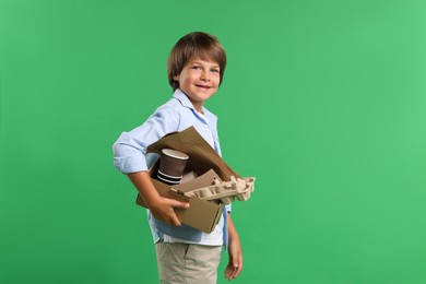 Photo of Recycling. Cute little boy with cardboard box full of different waste paper on green background