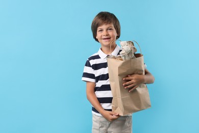 Photo of Recycling. Cute little boy with bag full of different waste paper on light blue background, space for text
