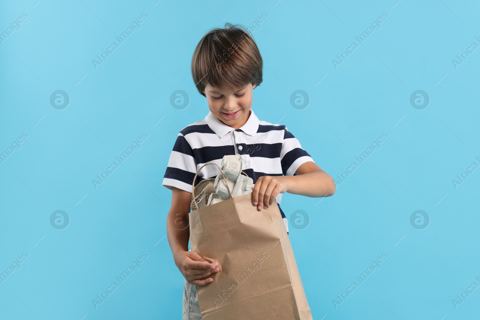 Photo of Recycling. Cute little boy with bag full of different waste paper on light blue background