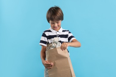 Photo of Recycling. Cute little boy with bag full of different waste paper on light blue background