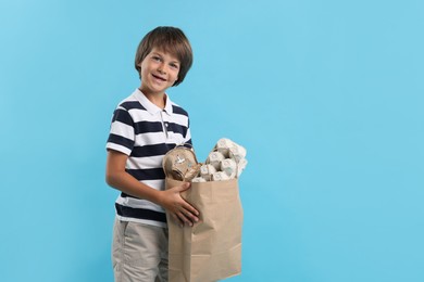 Photo of Recycling. Cute little boy with bag full of different waste paper on light blue background, space for text