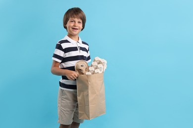 Photo of Recycling. Cute little boy with bag full of different waste paper on light blue background, space for text