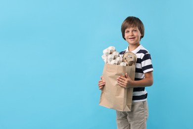 Photo of Recycling. Cute little boy with bag full of different waste paper on light blue background, space for text