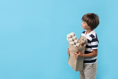 Photo of Recycling. Cute little boy with bag full of different waste paper on light blue background, space for text