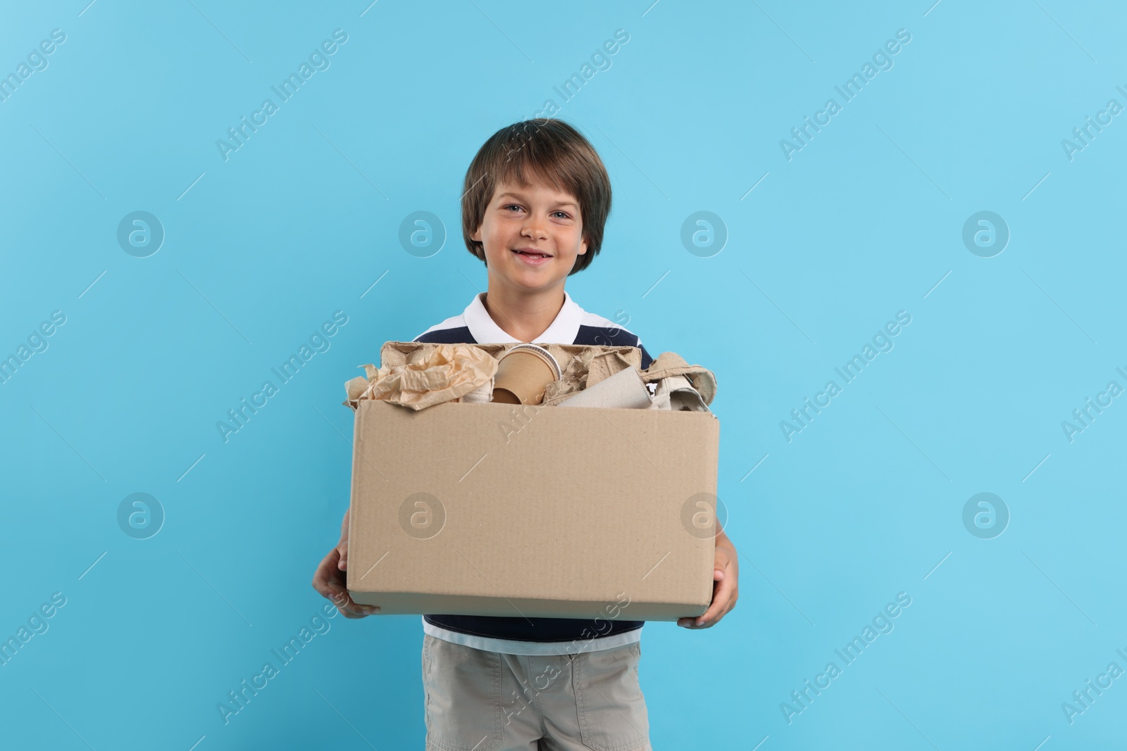 Photo of Recycling. Cute little boy with cardboard box full of different waste paper on light blue background