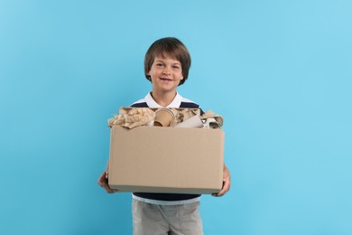 Photo of Recycling. Cute little boy with cardboard box full of different waste paper on light blue background