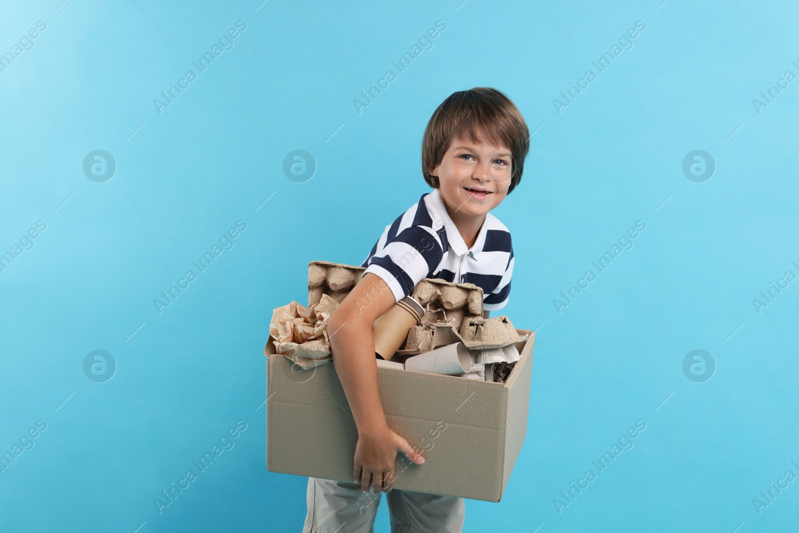 Photo of Recycling. Cute little boy with cardboard box full of different waste paper on light blue background