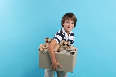 Photo of Recycling. Cute little boy with cardboard box full of different waste paper on light blue background