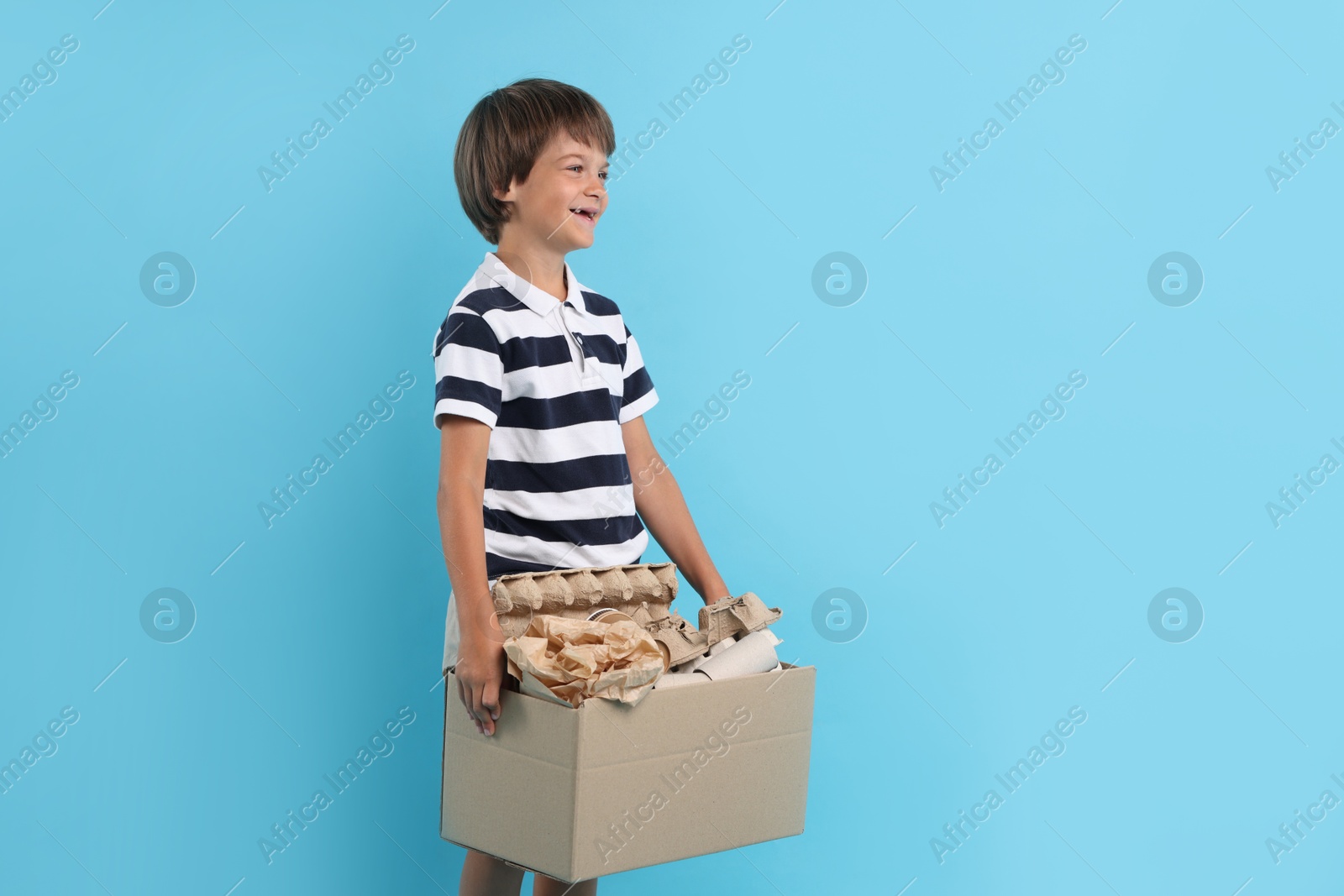 Photo of Recycling. Cute little boy with cardboard box full of different waste paper on light blue background