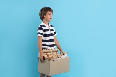 Photo of Recycling. Cute little boy with cardboard box full of different waste paper on light blue background