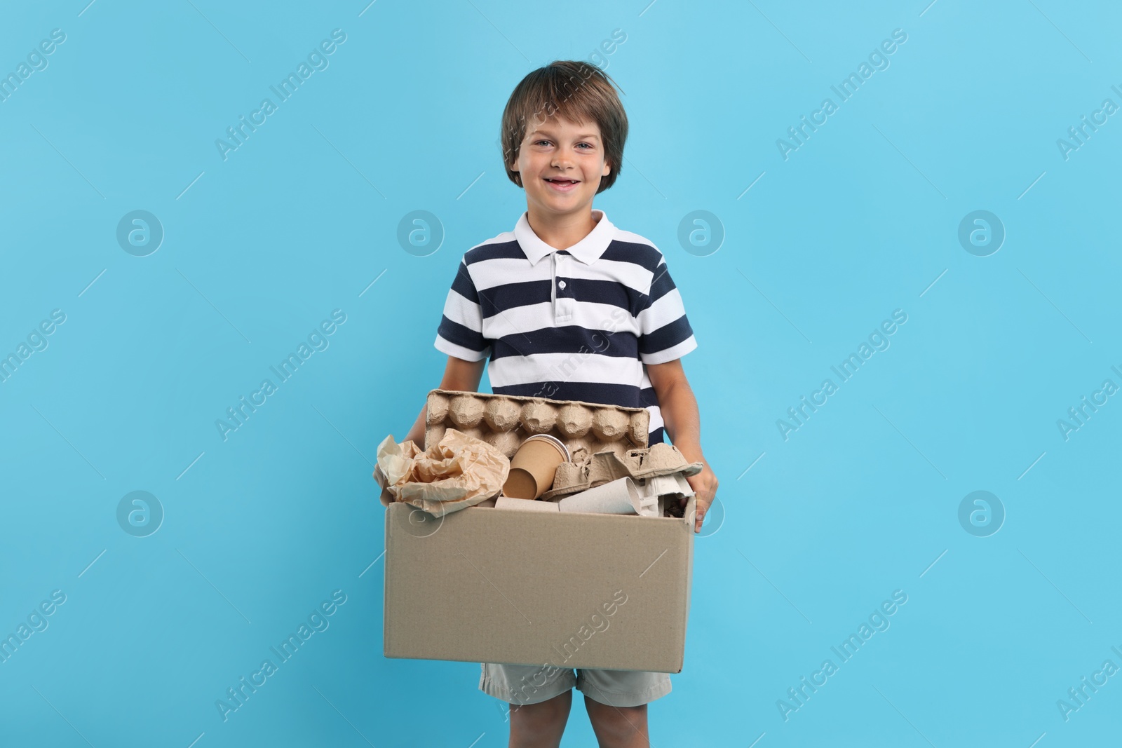 Photo of Recycling. Cute little boy with cardboard box full of different waste paper on light blue background