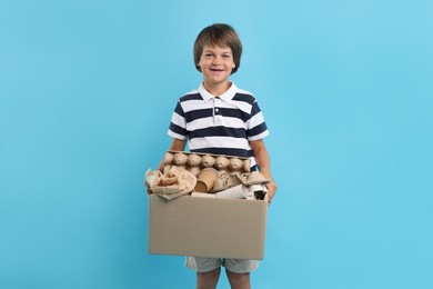 Photo of Recycling. Cute little boy with cardboard box full of different waste paper on light blue background