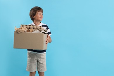 Photo of Recycling. Cute little boy with cardboard box full of different waste paper on light blue background, space for text