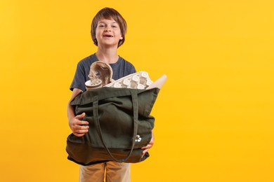 Photo of Recycling. Cute little boy with bag full of different waste paper on orange background, space for text
