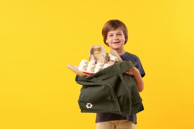 Photo of Recycling. Cute little boy with bag full of different waste paper on orange background, space for text