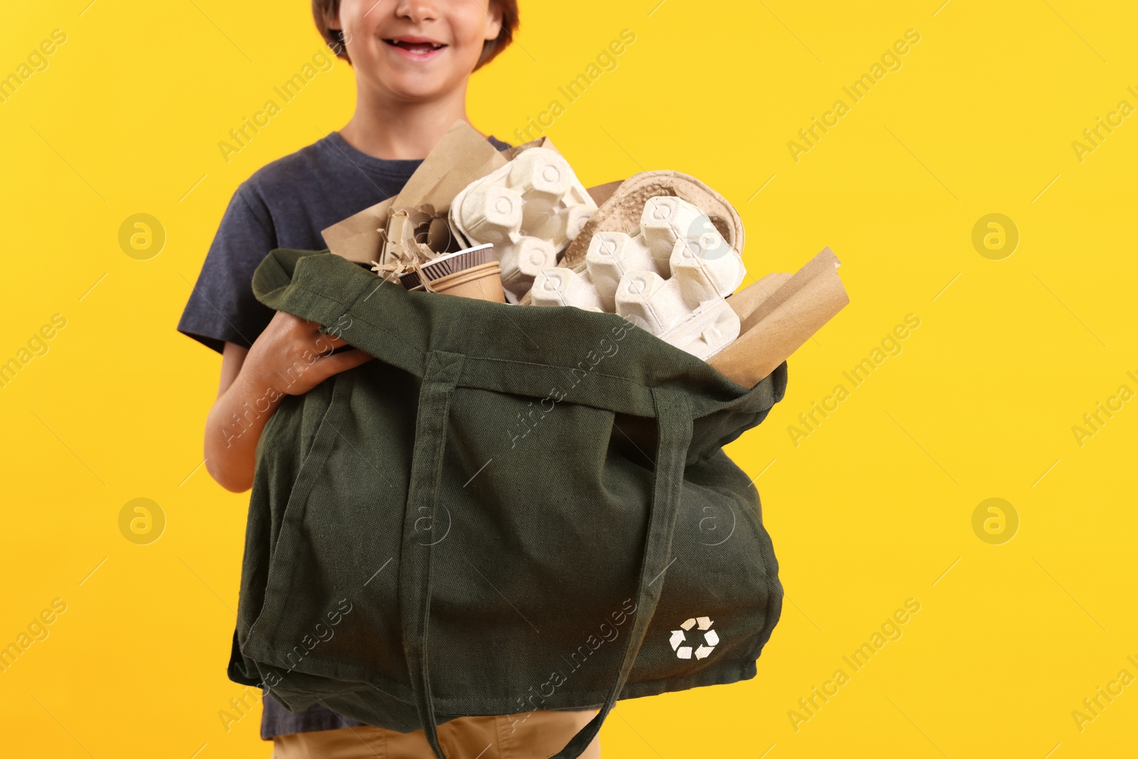 Photo of Recycling. Cute little boy with bag full of different waste paper on orange background, closeup. Space for text