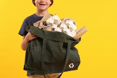 Photo of Recycling. Cute little boy with bag full of different waste paper on orange background, closeup. Space for text