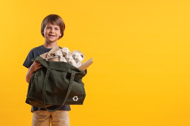 Photo of Recycling. Cute little boy with bag full of different waste paper on orange background, space for text