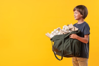 Photo of Recycling. Cute little boy with bag full of different waste paper on orange background, space for text