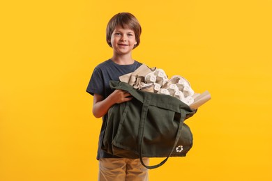 Photo of Recycling. Cute little boy with bag full of different waste paper on orange background