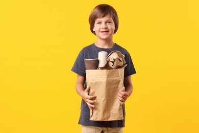 Photo of Recycling. Cute little boy with bag full of different waste paper on orange background