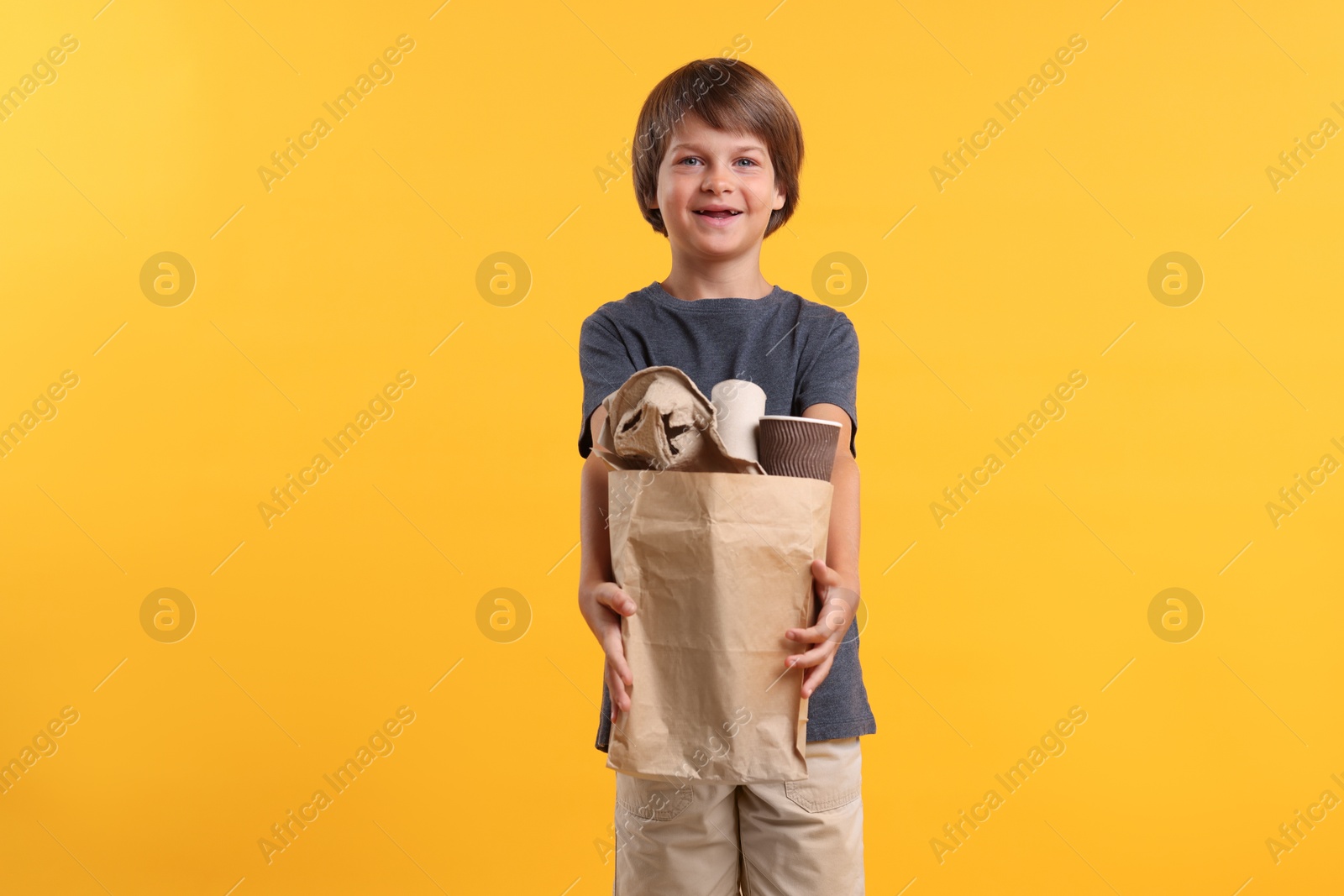 Photo of Recycling. Cute little boy with bag full of different waste paper on orange background