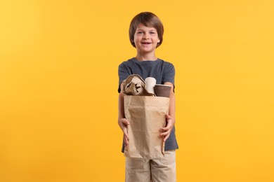 Photo of Recycling. Cute little boy with bag full of different waste paper on orange background