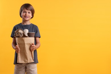 Photo of Recycling. Cute little boy with bag full of different waste paper on orange background, space for text