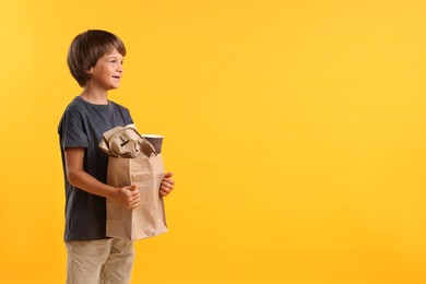 Photo of Recycling. Cute little boy with bag full of different waste paper on orange background, space for text