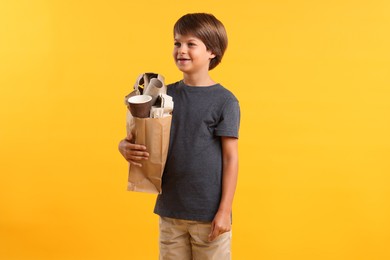 Photo of Recycling. Cute little boy with bag full of different waste paper on orange background