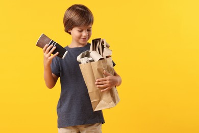 Photo of Recycling. Cute little boy with bag full of different waste paper on orange background, space for text
